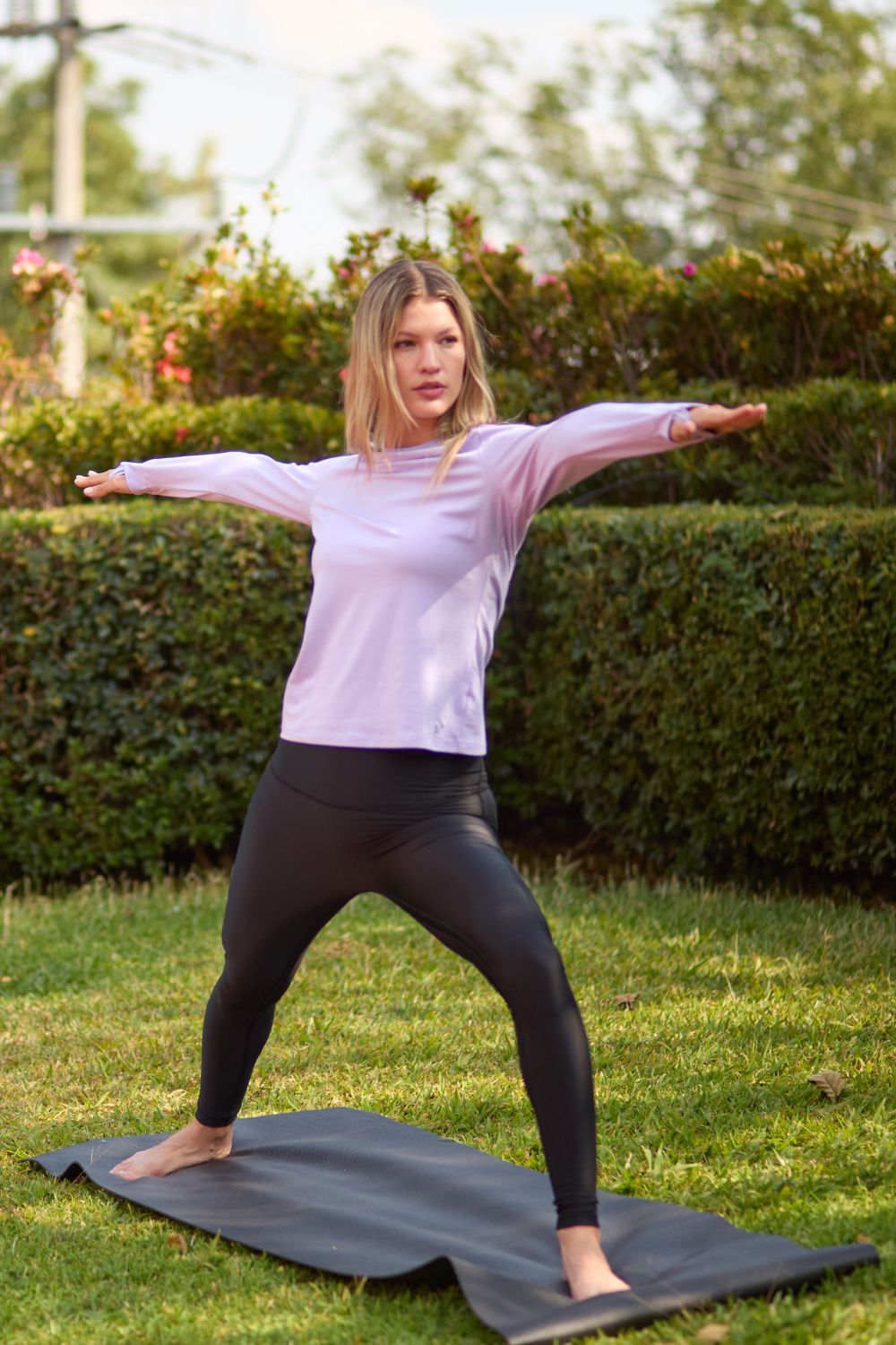 Femme en t-shirt anti-UV léger et manches longues, UPF 50+, pratiquant le yoga dans un jardin ensoleillé.